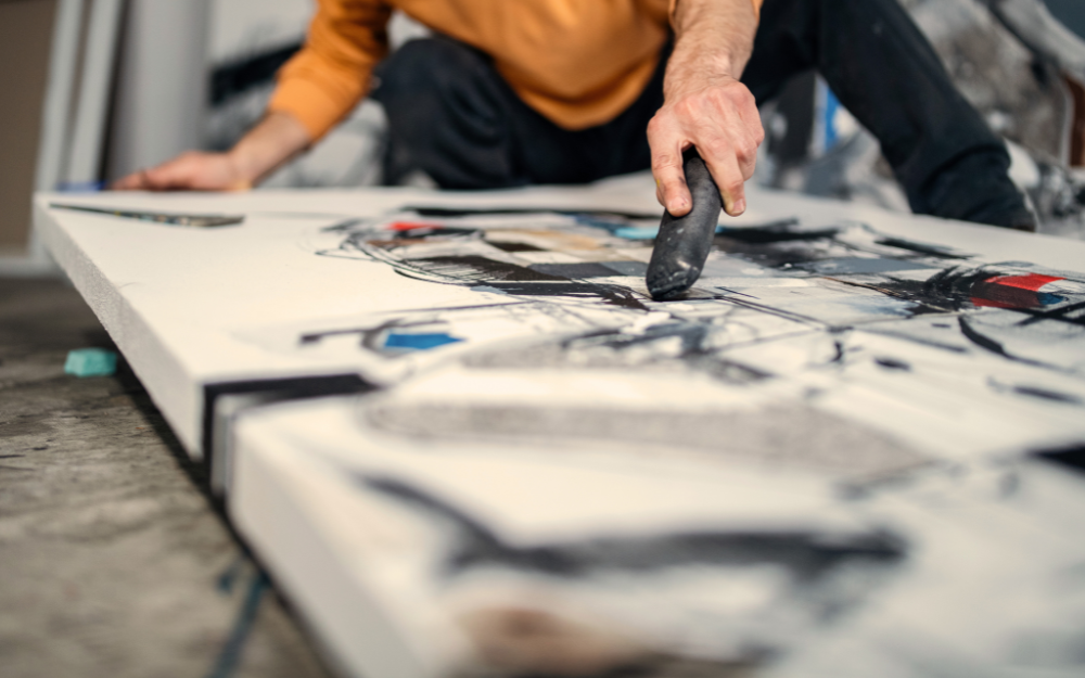 a person sits on the floor drawing on a large canvas with charcoal