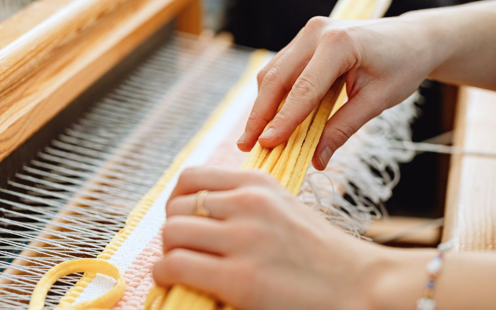 close up of a person's hands weaving on a loom